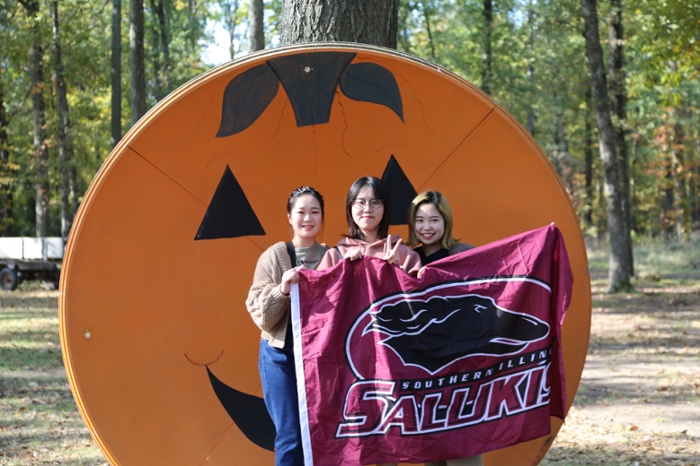 Student holding SUI flags in front of pumpkin sign